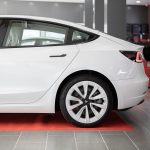 Carro elétrico branco exposto sobre um tapete vermelho dentro de um showroom automotivo.