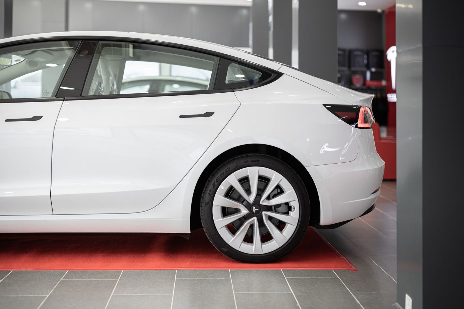 Carro elétrico branco exposto sobre um tapete vermelho dentro de um showroom automotivo.