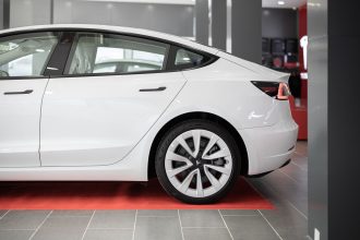 Carro elétrico branco exposto sobre um tapete vermelho dentro de um showroom automotivo.