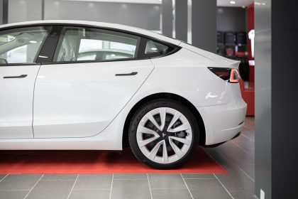 Carro elétrico branco exposto sobre um tapete vermelho dentro de um showroom automotivo.