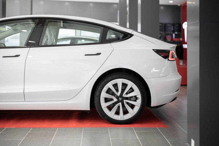 Carro elétrico branco exposto sobre um tapete vermelho dentro de um showroom automotivo.