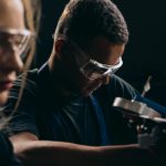 Estudantes usam óculos de proteção e trabalham juntos em um projeto de robótica em uma oficina.