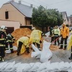 Equipe de emergência preenche sacos de areia em uma rua alagada durante a chuva.
