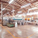 Vista ampla do interior organizado de uma fábrica brasileira, com máquinas industriais modernas.