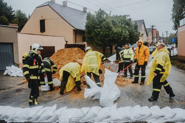 Equipe de emergência preenche sacos de areia em uma rua alagada durante a chuva.