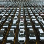 Vista aérea de um grande pátio com milhares de carros estacionados em fileiras.