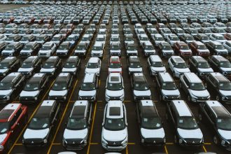 Vista aérea de um grande pátio com milhares de carros estacionados em fileiras.