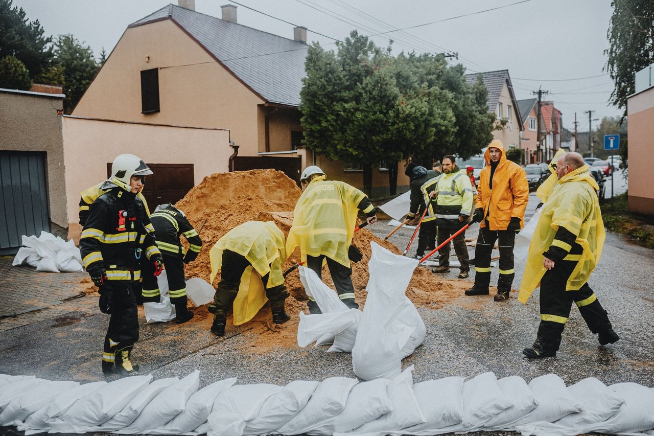 Equipe de emergência preenche sacos de areia em uma rua alagada durante a chuva.