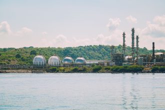Instalação industrial de armazenamento de gás, com tanques esféricos e chaminés junto ao litoral.
