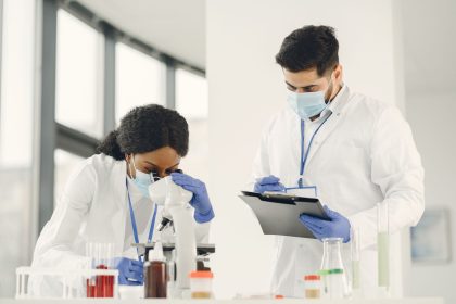 Dois cientistas trabalham em um laboratório, analisando uma amostra ao microscópio e consultando anotações.